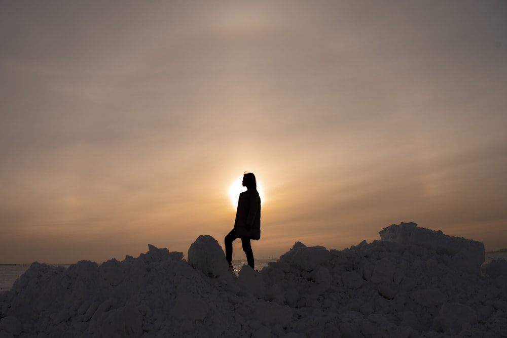 silhouette of woman standing on rocky mountain during sunset