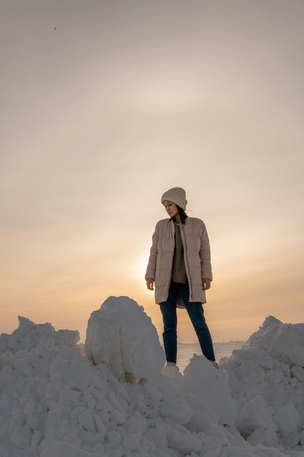 Person im braunen Mantel, die tagsüber auf einem weißen, schneebedeckten Berg steht