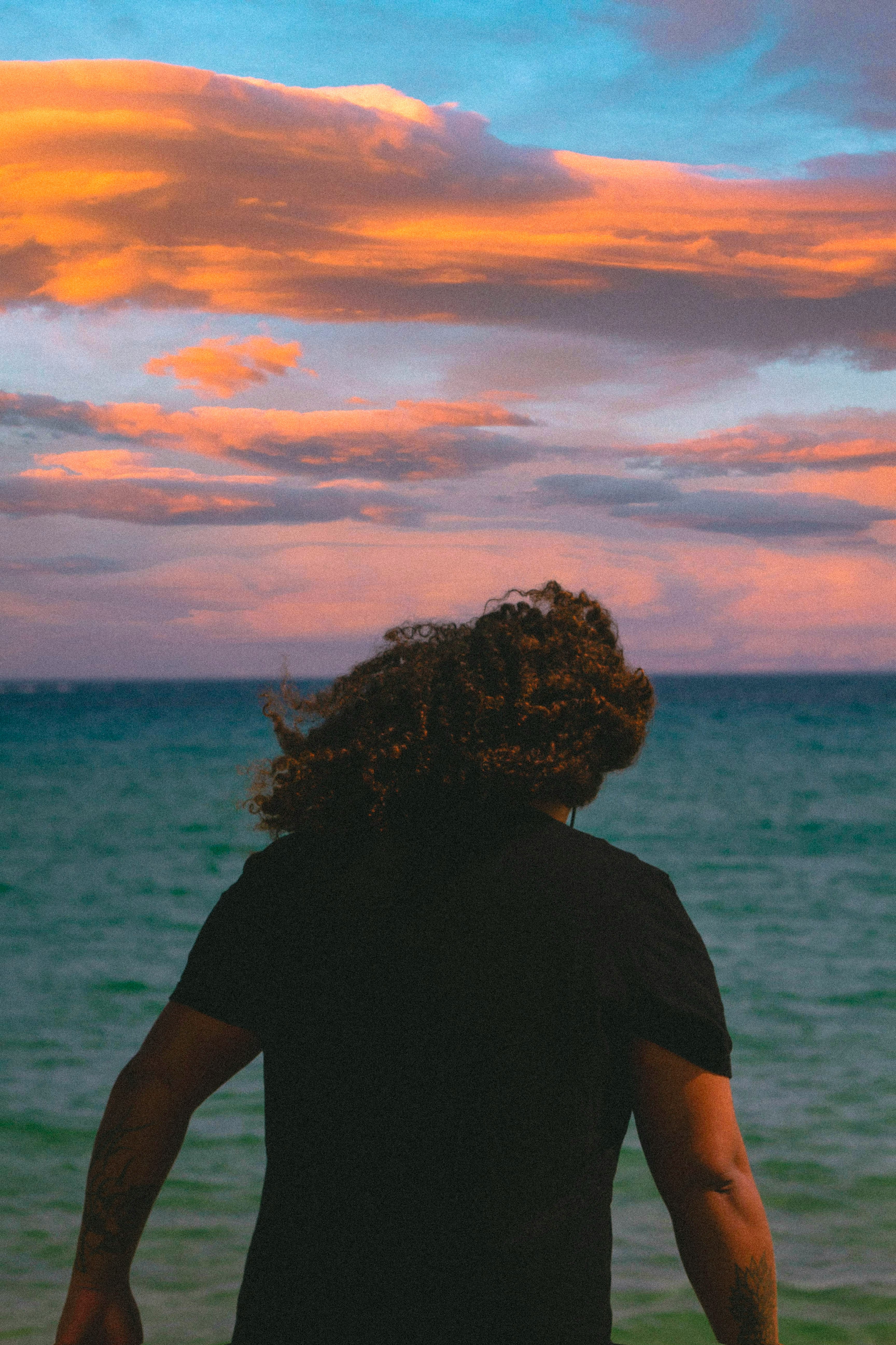 woman in black shirt standing near body of water during sunset