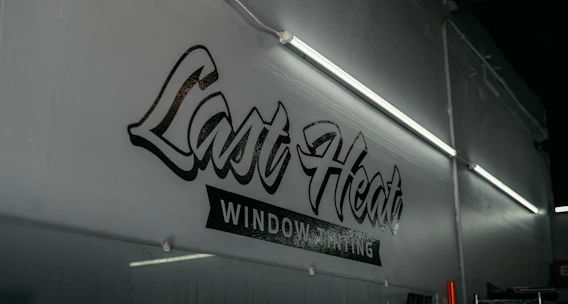 A technician carefully applying window tint film to a car door in a bright shop.