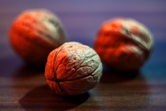 Three walnuts are placed on a wooden surface with a shallow depth of field. The focus is on the walnut in the foreground, highlighting its rugged texture and natural patterns.