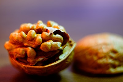 A close-up of an open walnut shell revealing the textured, brownish kernels inside. The background is blurred with warm lighting, highlighting the contours of the walnut.