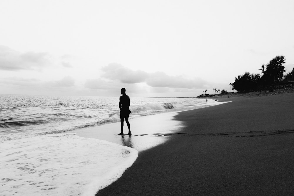 grayscale photo of man walking on beach