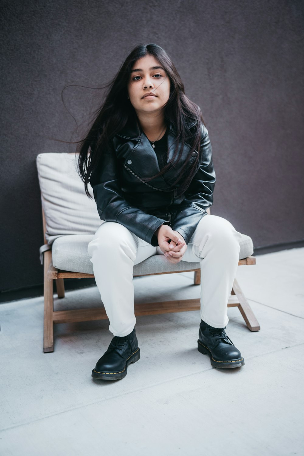 woman in black leather jacket and white pants sitting on white couch