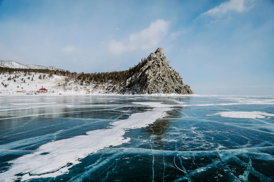 Serene winter landscape features jagged rock formation and frozen lake with blue-green ice