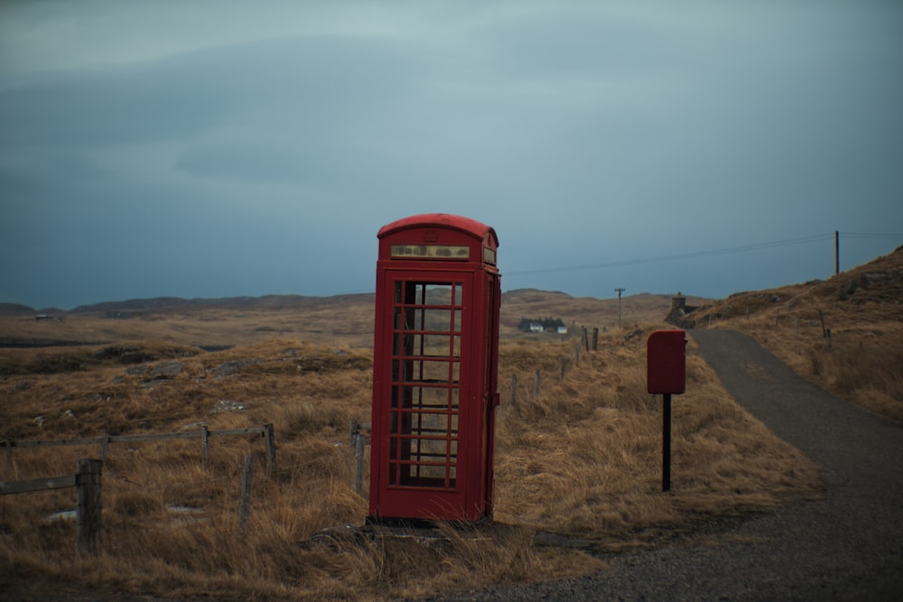 昼間の青空の下、茶色の芝生に赤い電話ボックス
