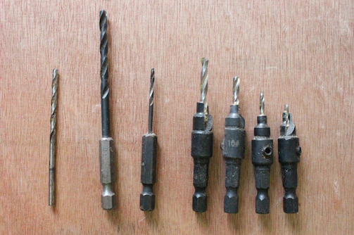 Electric drill with drill bits laid out beside it on a concrete floor.