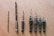 Seven drill bits of varying sizes are lined up on a wooden surface. The bits have a metallic sheen and appear to be well-used, with some showing signs of wear.