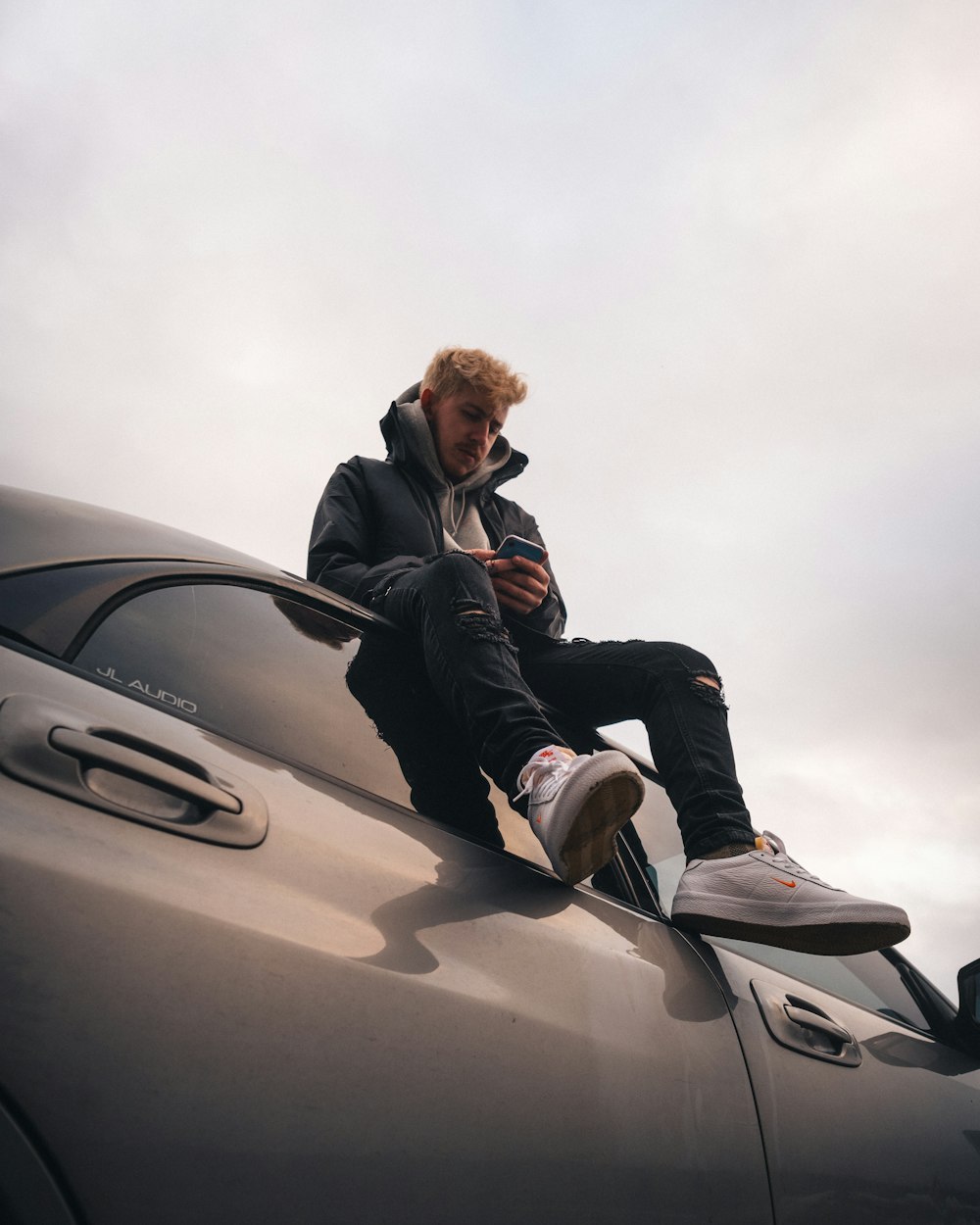 man in black suit jacket sitting on car hood during daytime