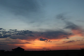 Sunset over a quiet rural landscape with scattered farm buildings and rolling hills