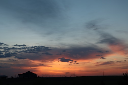 Sunset over a rural landscape with a silhouette of a cowboy hat on a fence post.