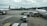 Airplanes are parked on an airport tarmac with airport ground handling vehicles and personnel around them. One plane has a colorful livery promoting 'Sustainable ASEAN Tourism', while another displays airline branding. The scene includes overcast skies and distant background buildings.