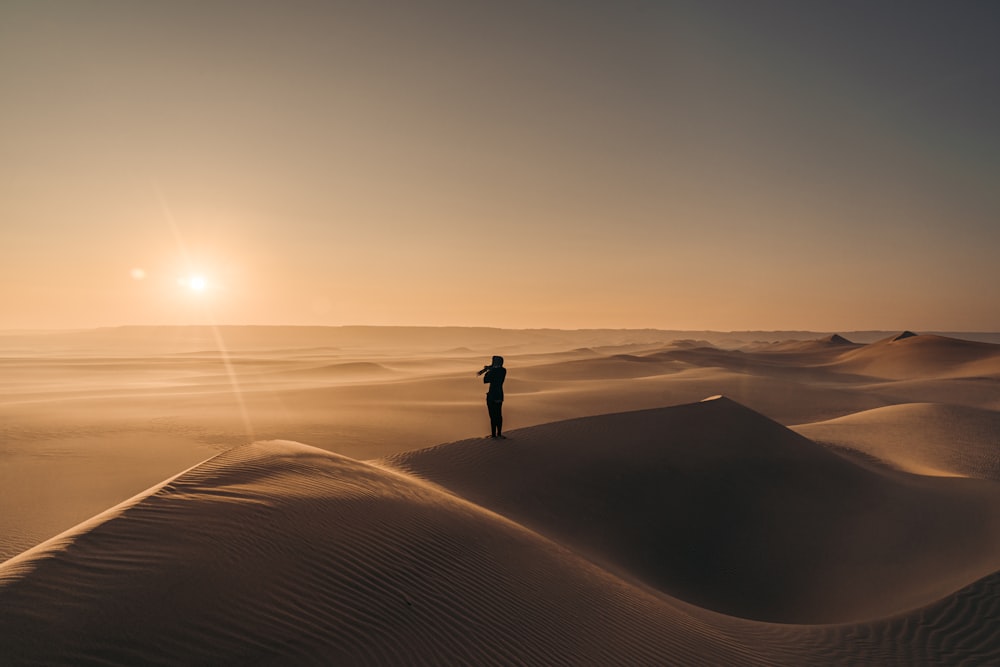 silhouette of person standing on sand during sunset