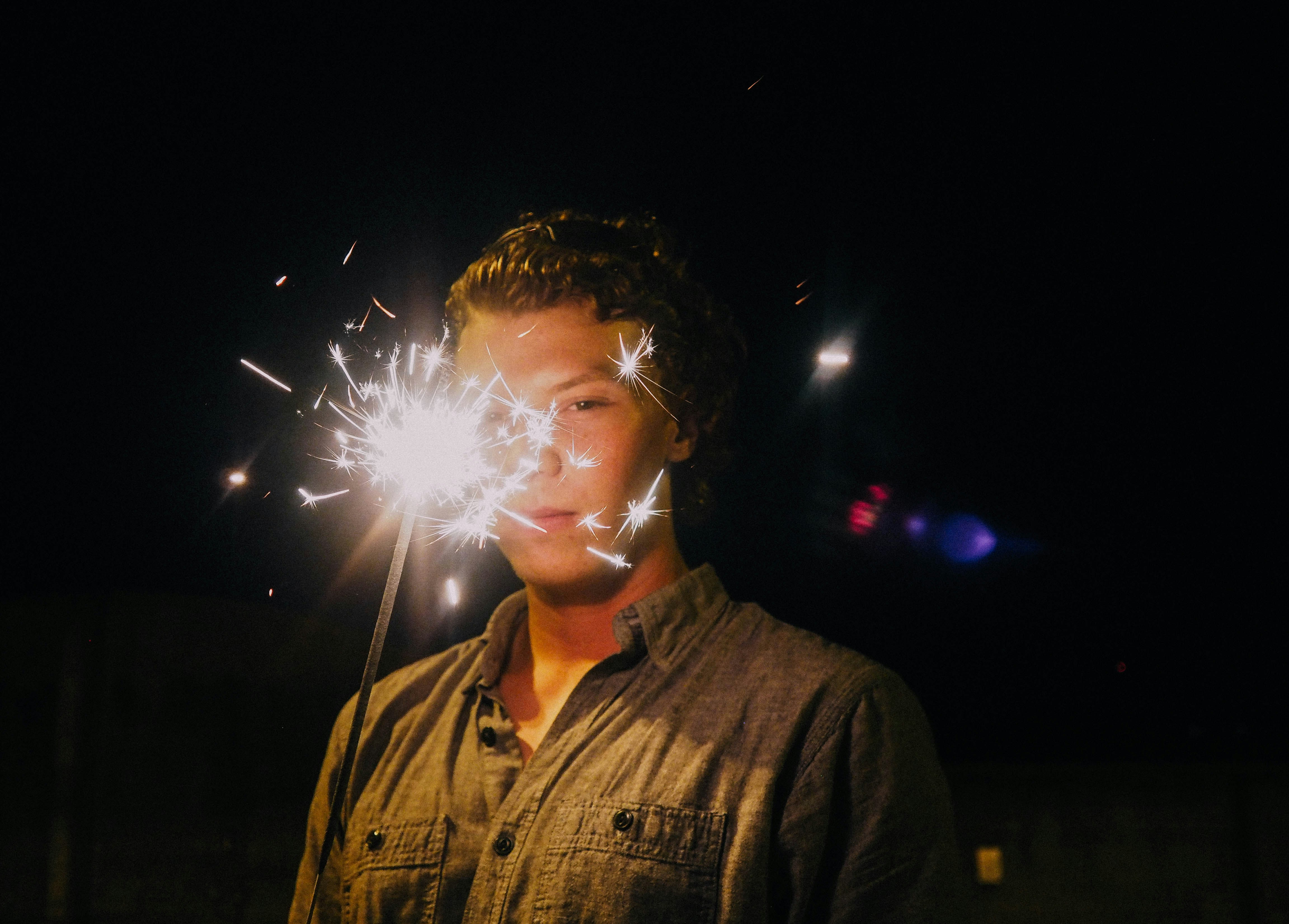 Homme en jean bleu boutonné jusqu’à la veste tenant des feux d’artifice blancs pendant la nuit