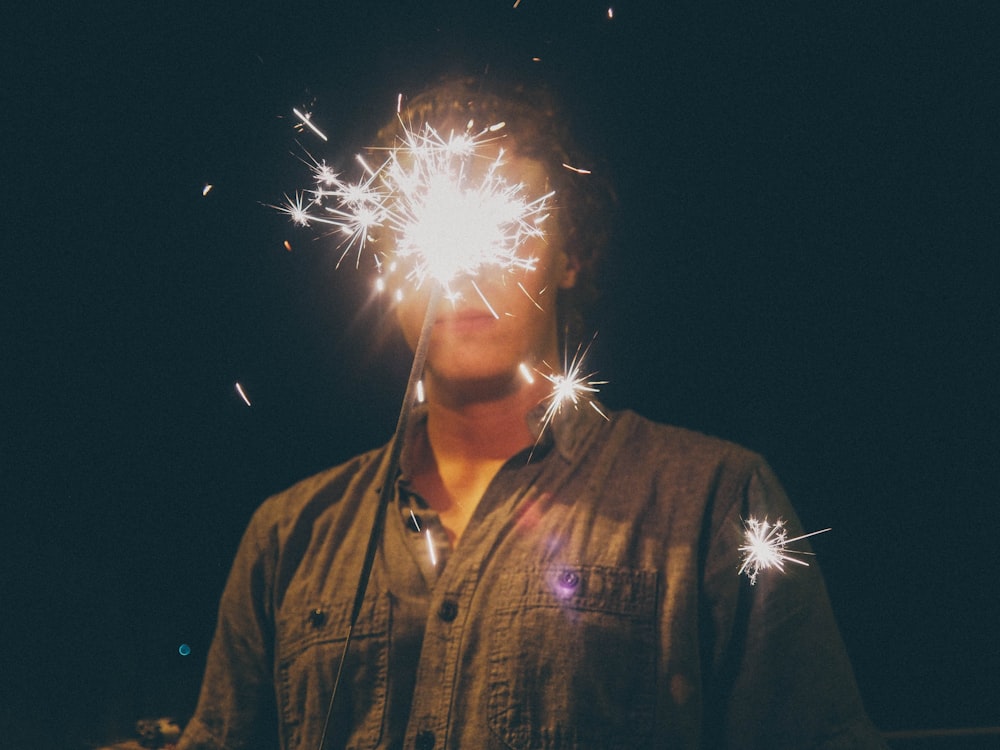 Hombre con camisa negra abotonada sosteniendo fuegos artificiales blancos