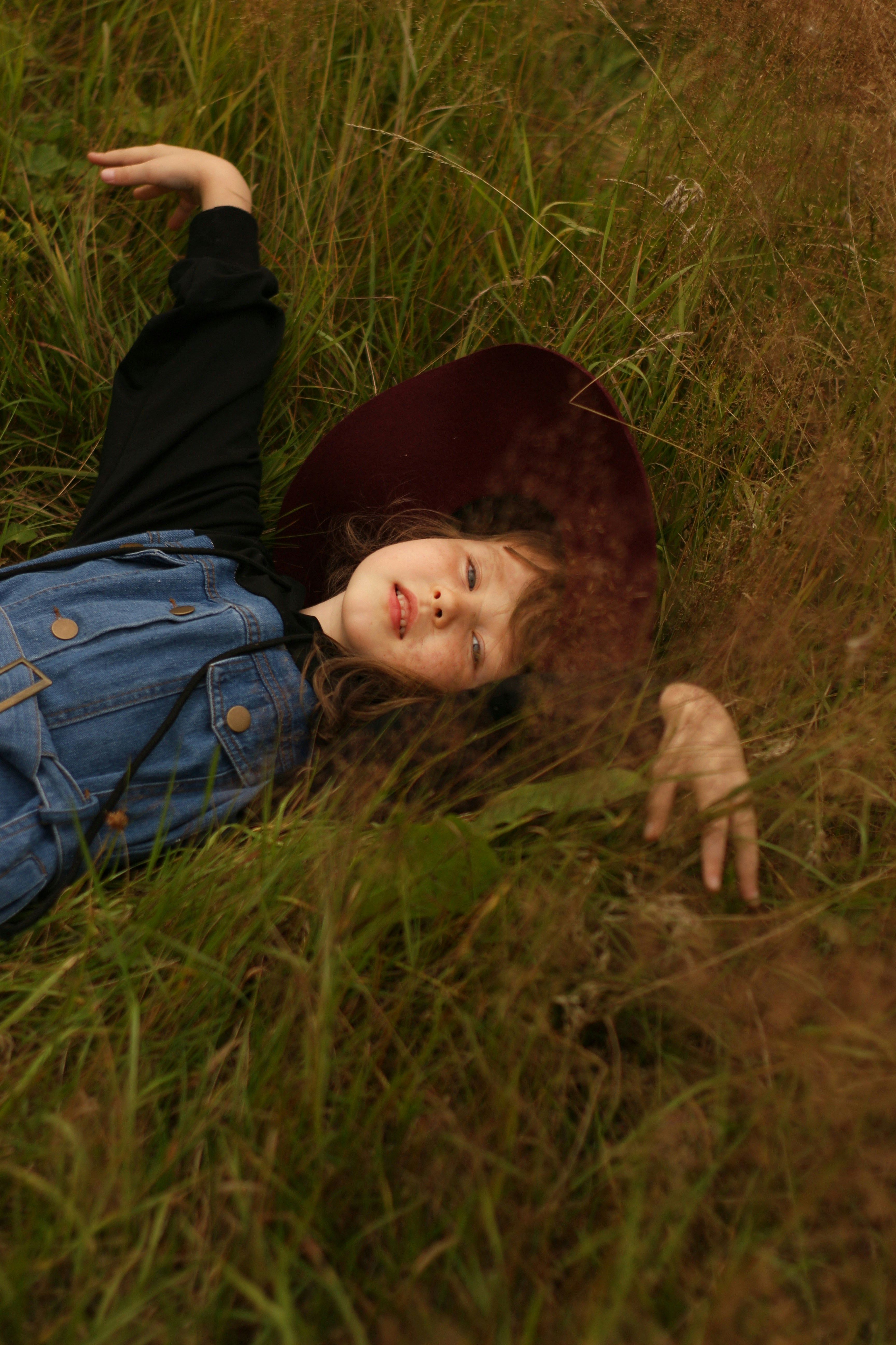 child in blue denim jacket lying on green grass field