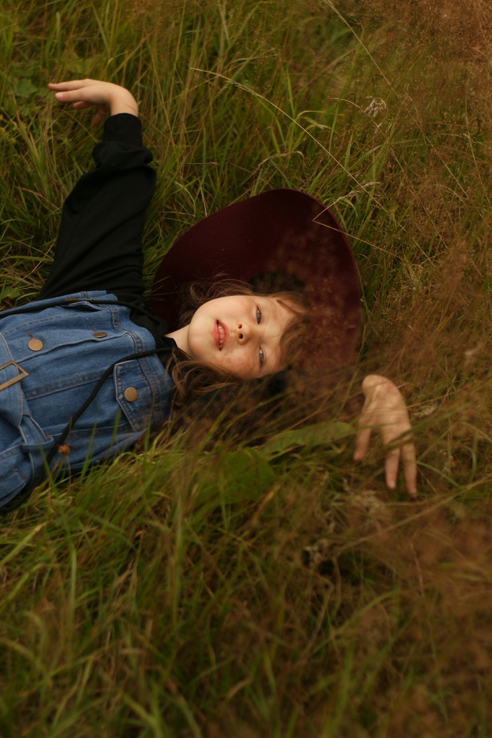 child in blue denim jacket lying on green grass field