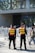 Two security personnel wearing reflective vests stand in front of a crowd, near barricades, outside the Shanghai Natural History Museum. The scene is busy with many people around, and the building's glass facade and signage are visible.