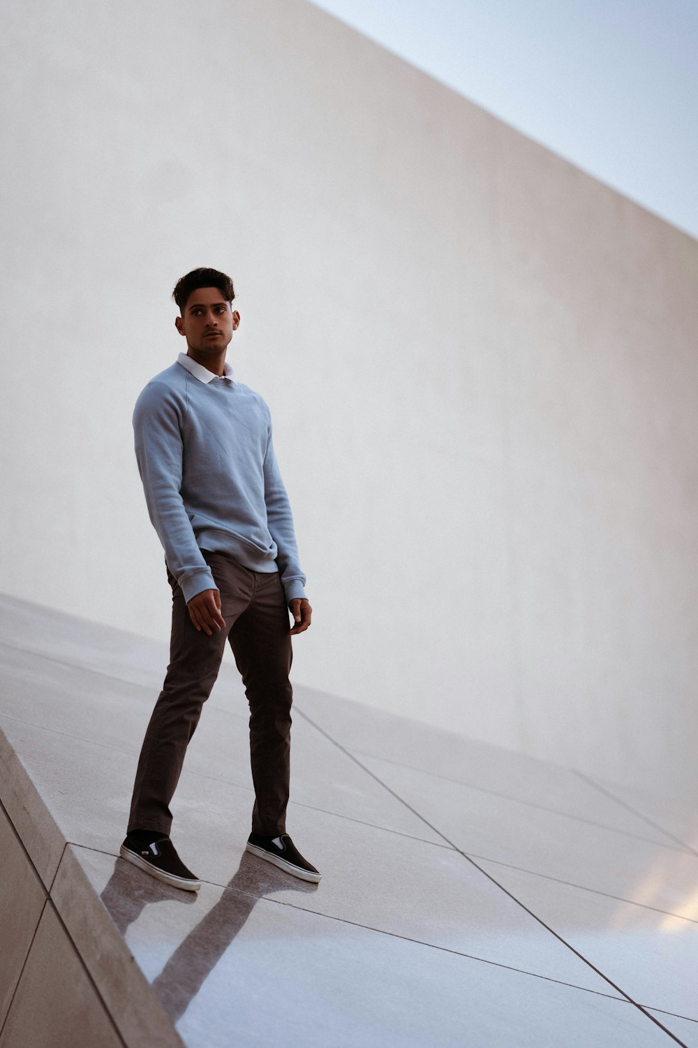 man in blue dress shirt and black pants standing on white floor tiles