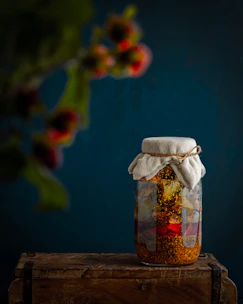 Close-up of a rustic glass jar filled with vibrant homemade mango pickle on a wooden table.