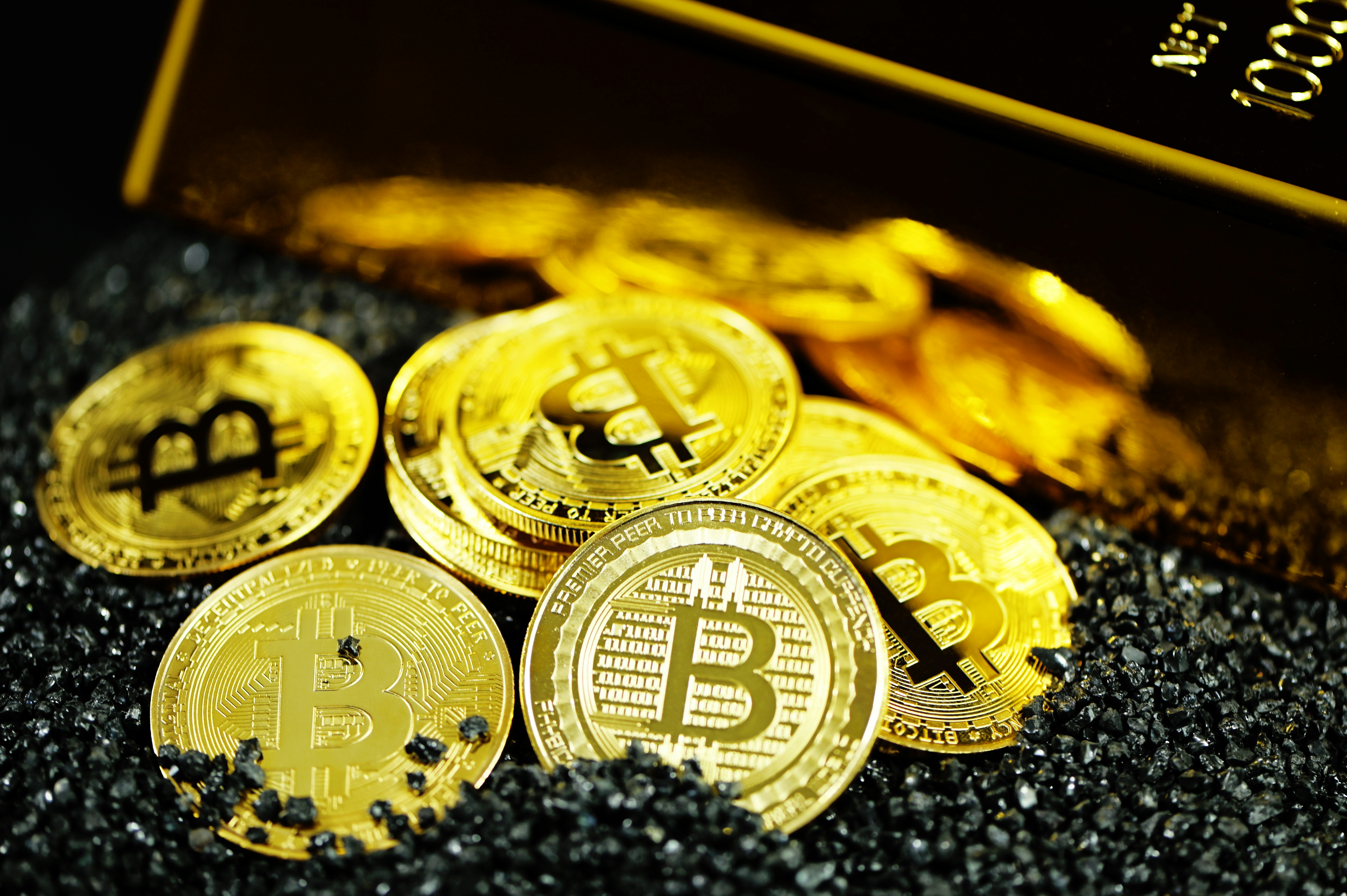 A pile of Bitcoins next to a gold bullion.