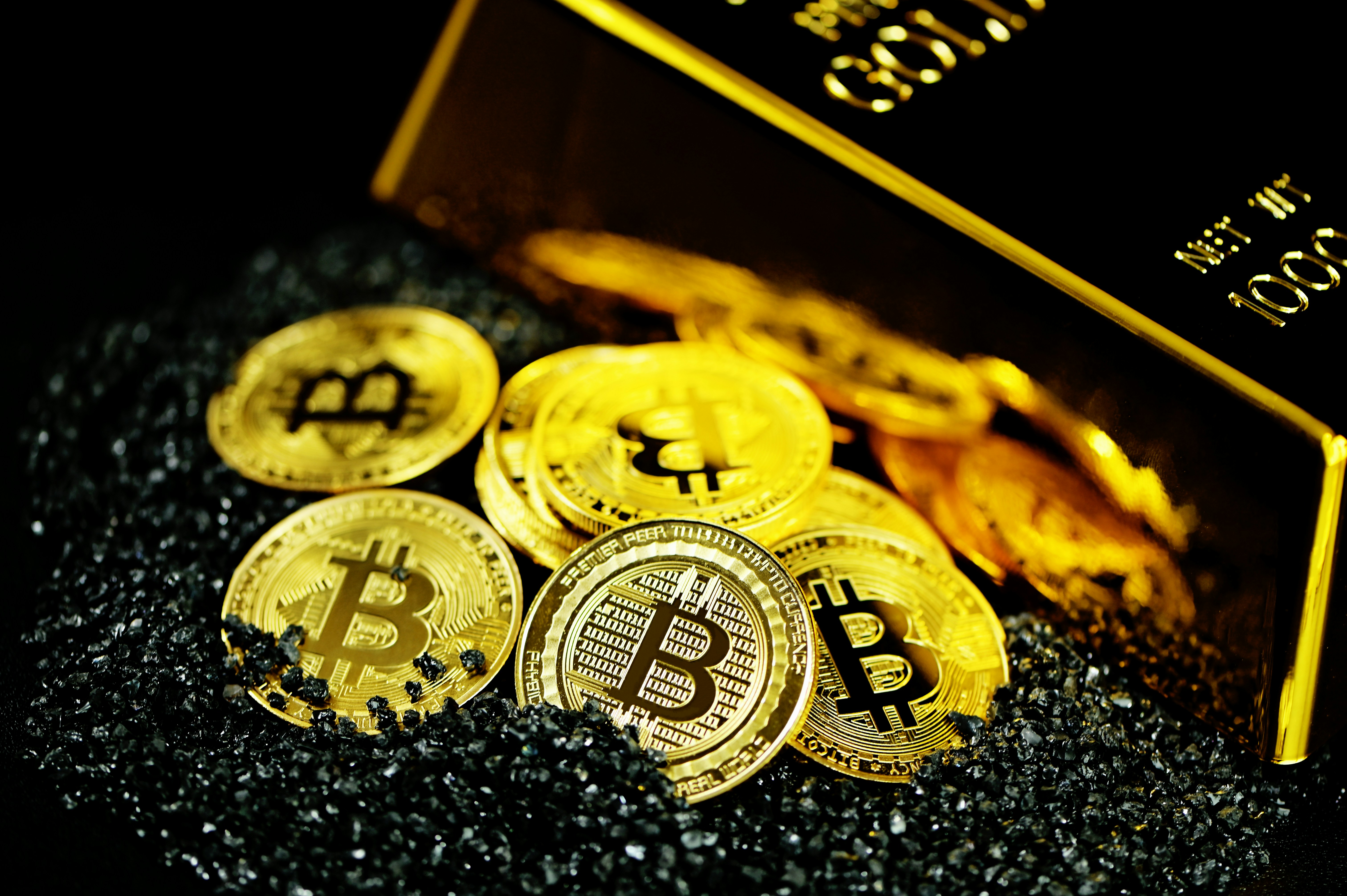 A pile of Bitcoins on black crystals next to a gold bullion