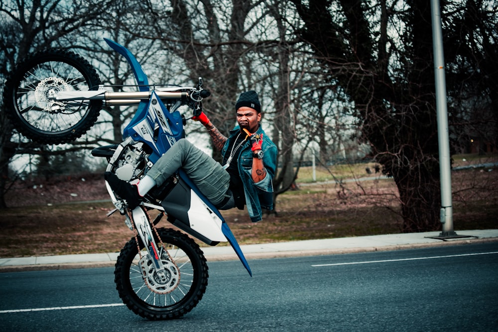 青と白のオートバイに乗る黒いジャケットの男性