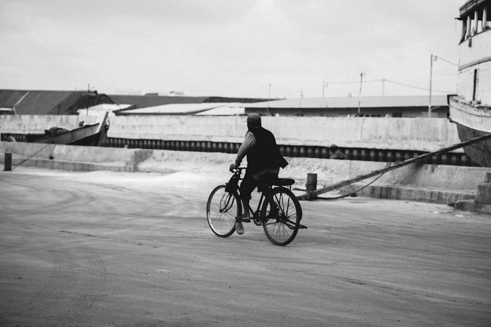 grayscale photo of man riding bicycle on road