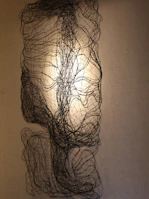 An abstract kinetic installation casting dynamic shadows on a white gallery wall.