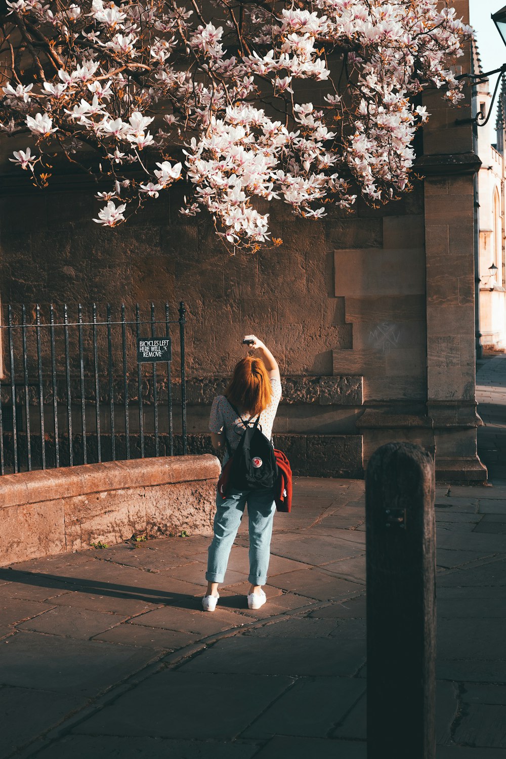 woman in black jacket and blue denim jeans standing on sidewalk during daytime