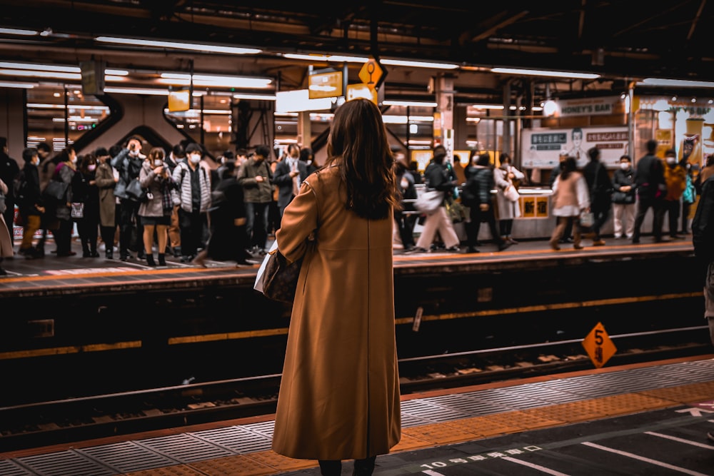 woman in brown coat walking on sidewalk during daytime