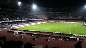 A sleek, modern soccer stadium under evening lights with players warming up on the field.