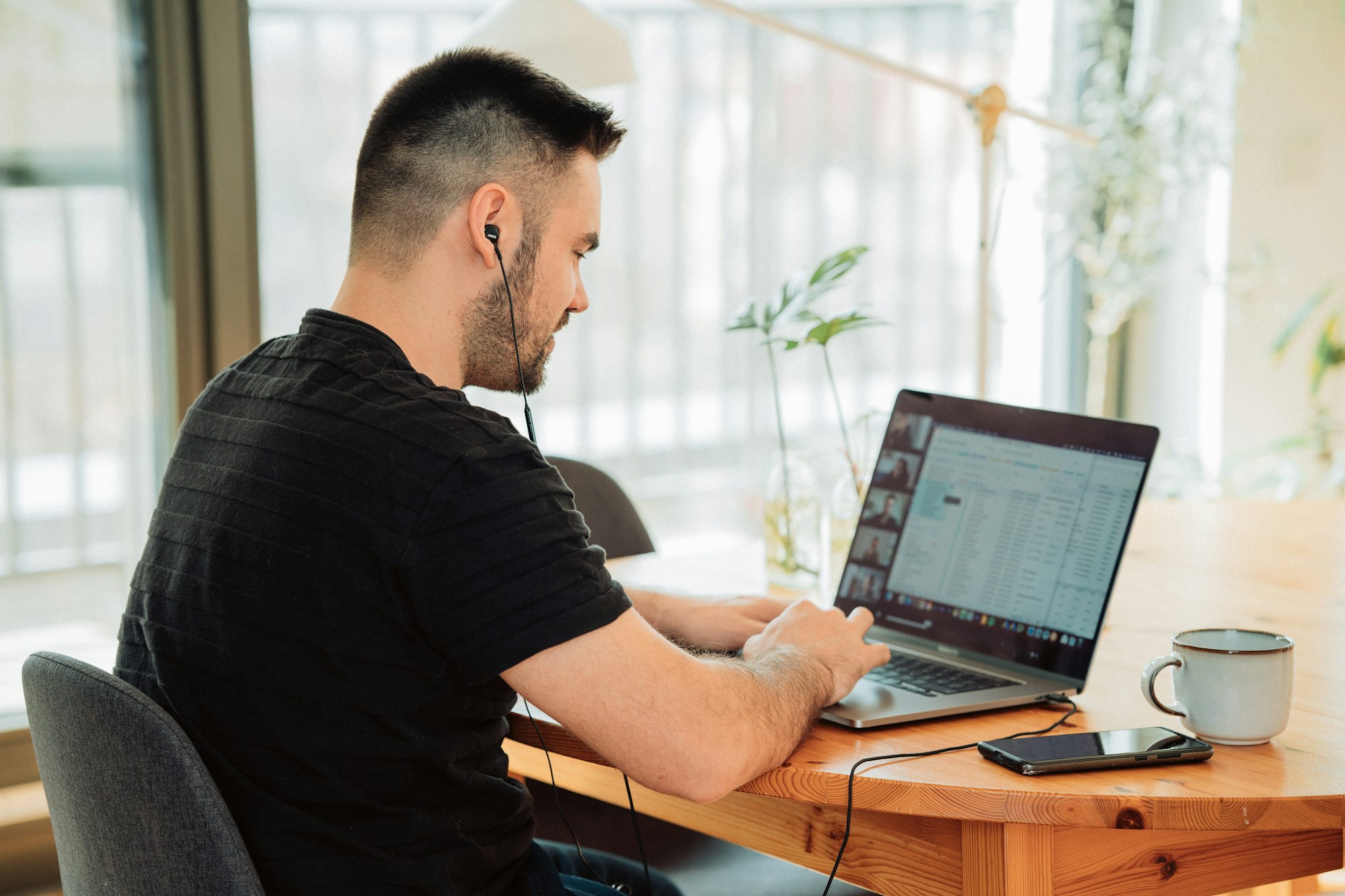 Homeoffice with macbook and phone and in ear headphones plugged in. Showing a young man working in home office and having a meeting conference via zoom hangout or gotomeeting. Or maybe having a webinar
