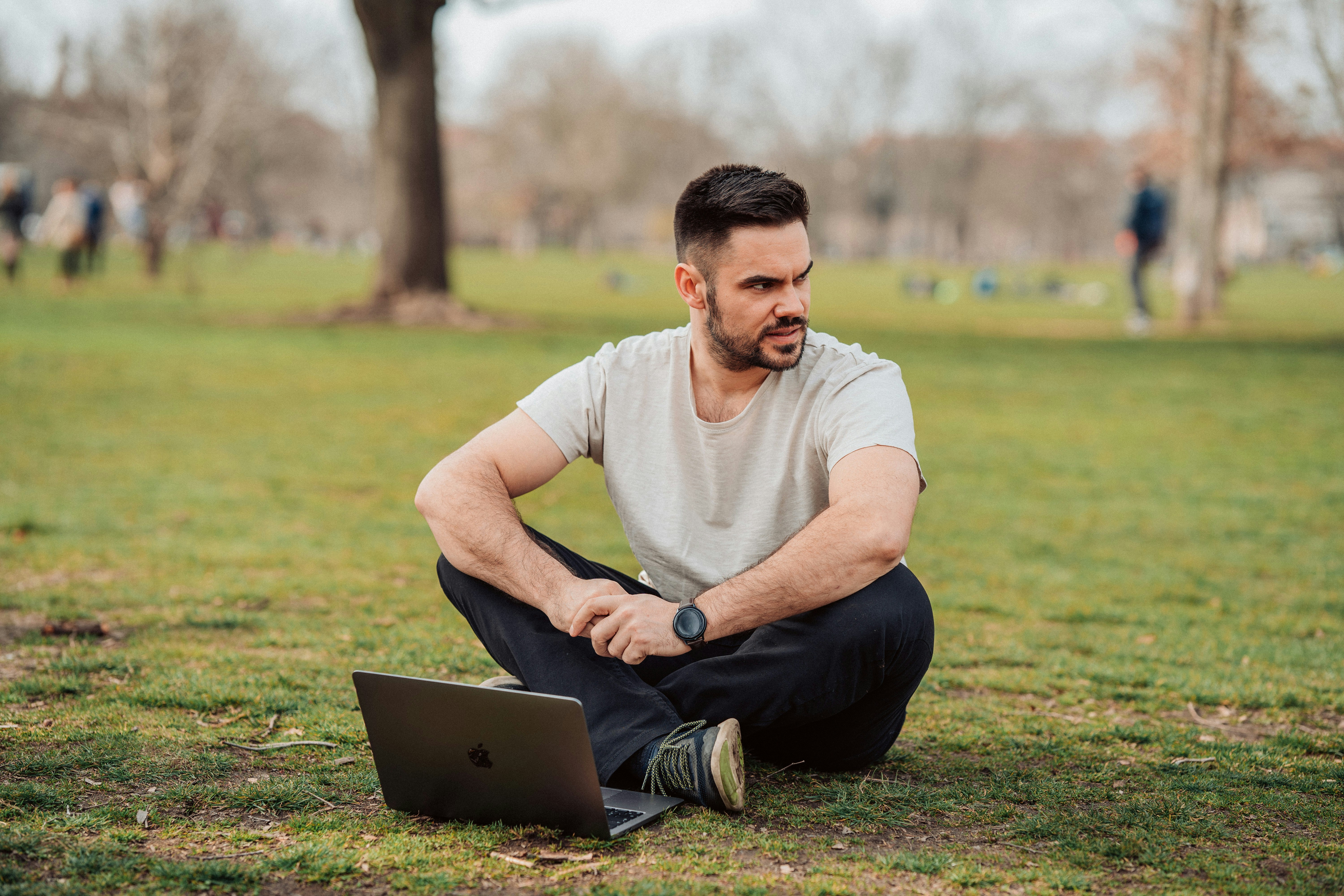 Having a webinar in the park. A man with his small laptop macbook air m1 chip sitting in the park.