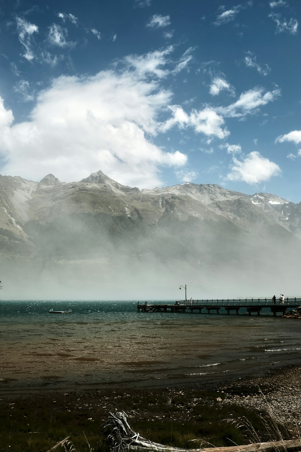 people walking on beach near mountain under white clouds during daytime