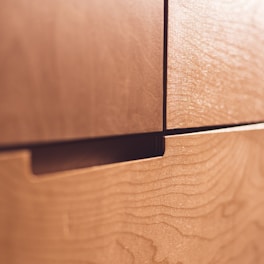A close-up view of wooden drawers with a natural, smooth finish. The grain pattern is visible on the surface, contributing to the texture and warmth of the wood.