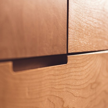 A close-up view of wooden drawers with a natural, smooth finish. The grain pattern is visible on the surface, contributing to the texture and warmth of the wood.