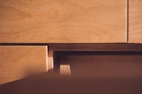 Wooden surfaces of plywood sheets are closely stacked with visible grain patterns and layered textures. The light casts a warm glow, highlighting the natural wood tones.