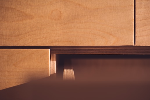 Wooden surfaces of plywood sheets are closely stacked with visible grain patterns and layered textures. The light casts a warm glow, highlighting the natural wood tones.