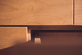 Wooden surfaces of plywood sheets are closely stacked with visible grain patterns and layered textures. The light casts a warm glow, highlighting the natural wood tones.