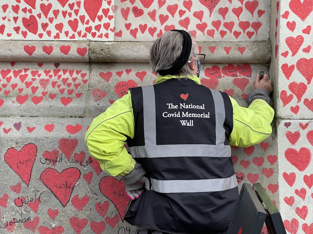 Femme en veste jaune et noire debout à côté d’un mur rouge et blanc