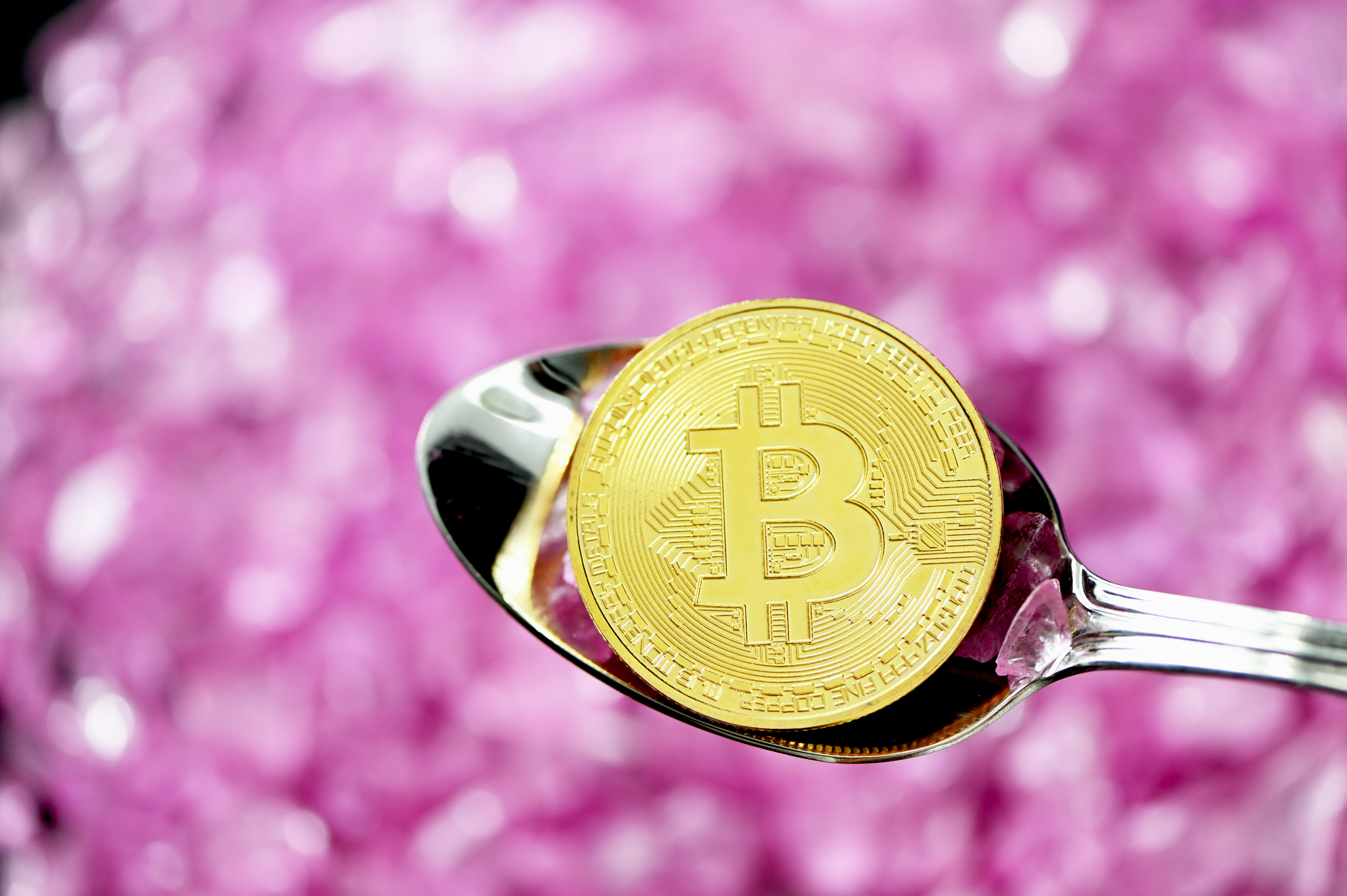 A golden bitcoin coin on the spoon and pink crystals