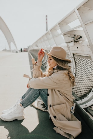 woman in brown coat and blue denim jeans sitting on gray metal bench during daytime