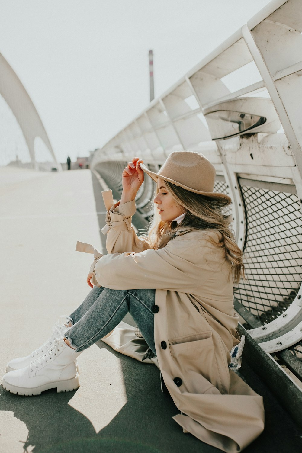 woman in brown coat and blue denim jeans sitting on gray metal bench during daytime