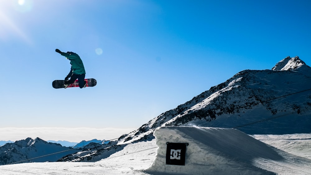 Persona in giacca verde e pantaloni neri che cavalca lo snowboard nero sulla montagna coperta di neve durante il giorno