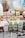 A selection of Foodie Flavours natural flavoring boxes are displayed on a wooden surface. Various flavors such as Rose, Apple, Lime, Pistachio, Organic Orange Oil, Apricot, Lemon, and Pineapple are showcased. In the background, there are baking ingredients like a measuring cup with brown sugar, a large mixing bowl with dough, a jug of milk, and colorful cupcake liners.