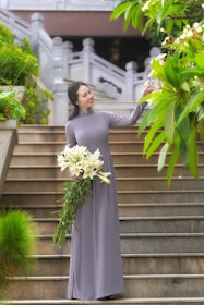 woman in gray sleeveless dress holding bouquet of white flowers standing on gray concrete stairs
