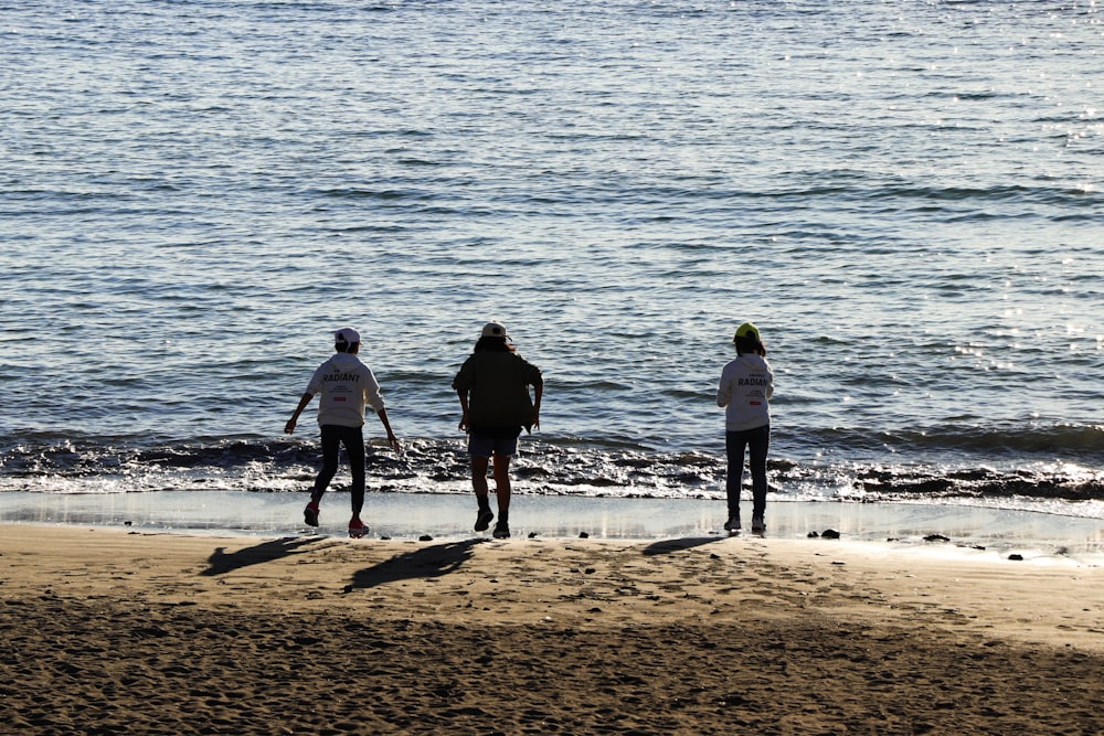 3 men standing on beach during daytime