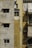 Old apartment building exterior with weathered and stained walls. The left side is pale gray with two small windows covered by awnings. The middle section is a faded yellow with clothes hanging near a small window and an air conditioning unit below. The right section has whitish sheets or curtains covering windows, with more stains becoming visible under sunlight.