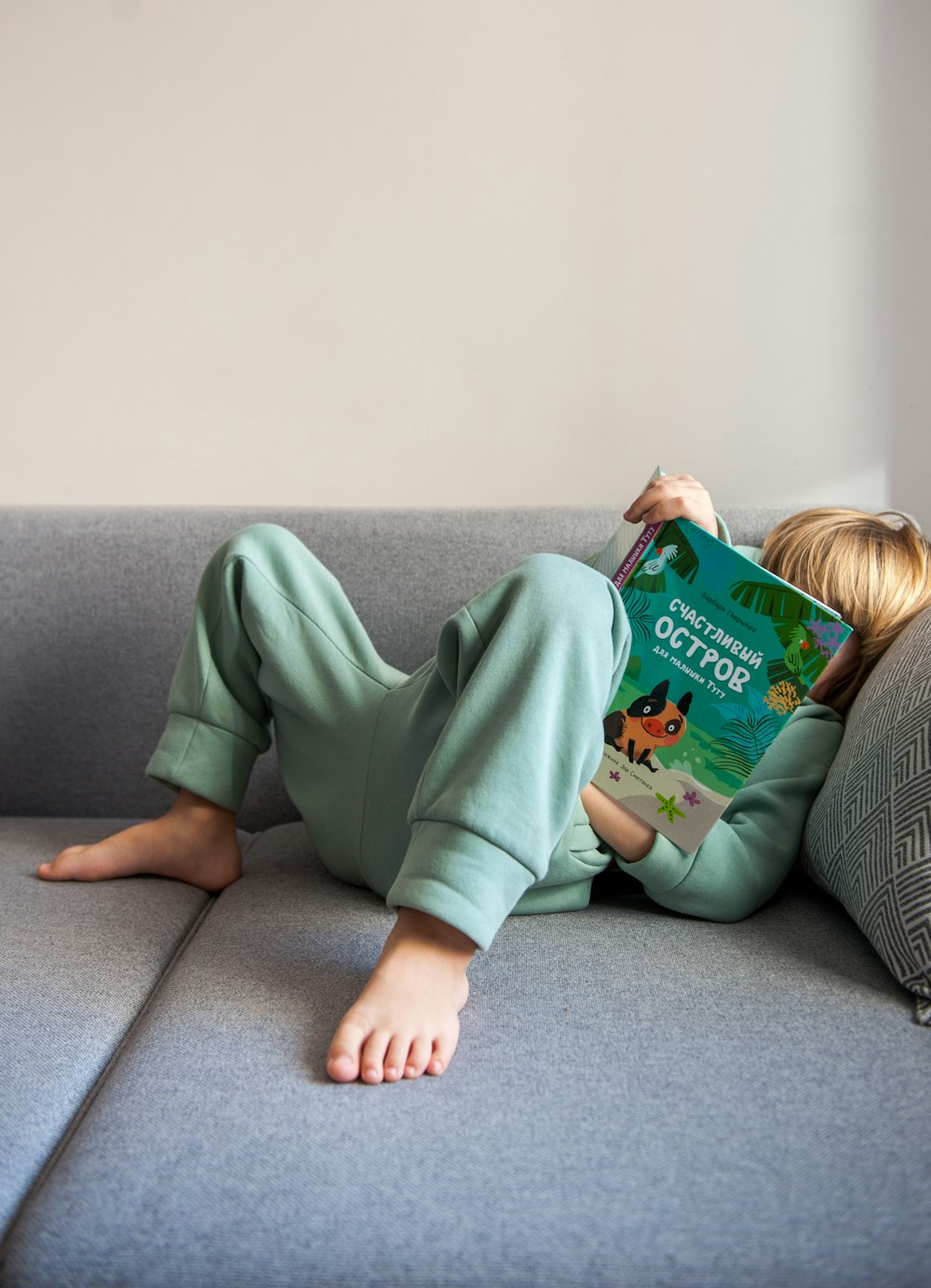 girl in green long sleeve shirt lying on gray couch